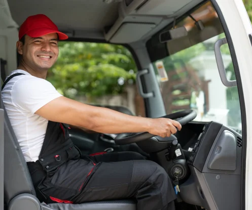 Smiling man wearing a red cap, sitting behind the wheel of a truck, enjoying the drive