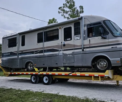 Truck towing an RV on a flatbed, moving along the road
